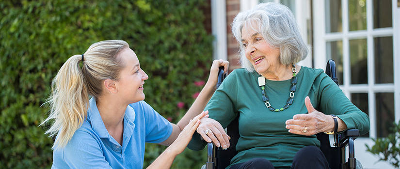 Image of a care partner kneeling in front of a patient in a wheelchair listening to her speak.