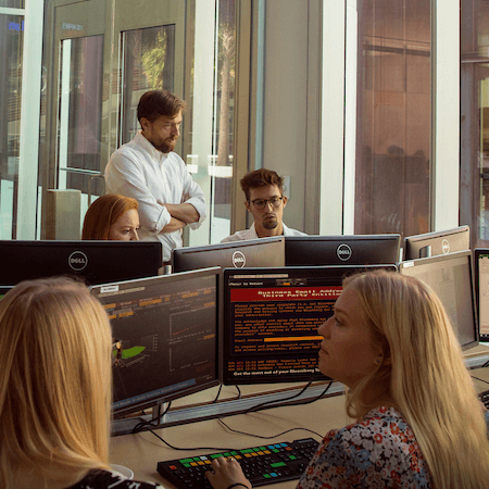 a man is standing up and teaching a group of students in a computer lab. the man is teaching group of students who are sitting at computers in the lab.