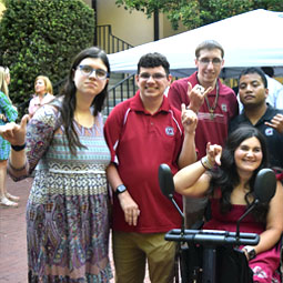 Group of students giving the "Spurs Up" sign with thumb and pinky outspread, the other fingers clenched. A student on the lower right is in a wheelchair.
