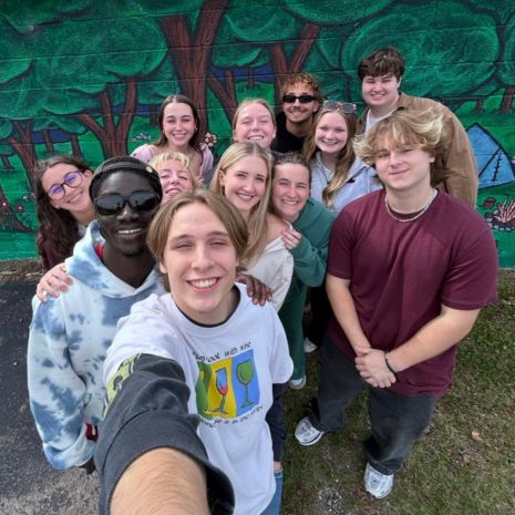 Group of students pose for photo in front of mural