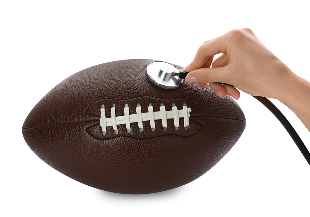 A hand holds a stethoscope to an American football.