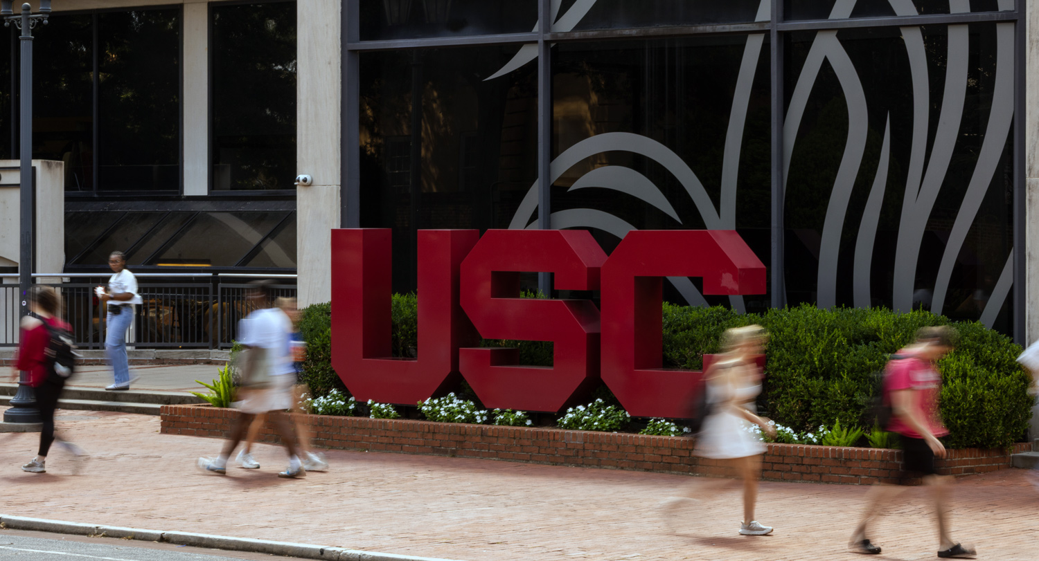 a building with the letters USC in front of windows with people walking in the foreground