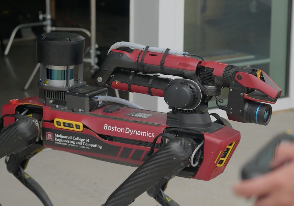 a robot "dog" with a hand holding a remote in the foreground