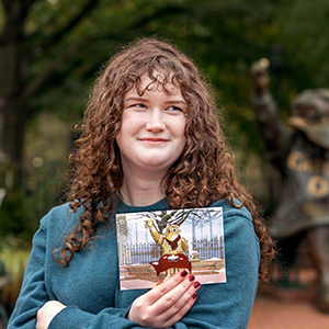 Audrey Webb holds a copy of her winning artwork in front of the Cocky statue